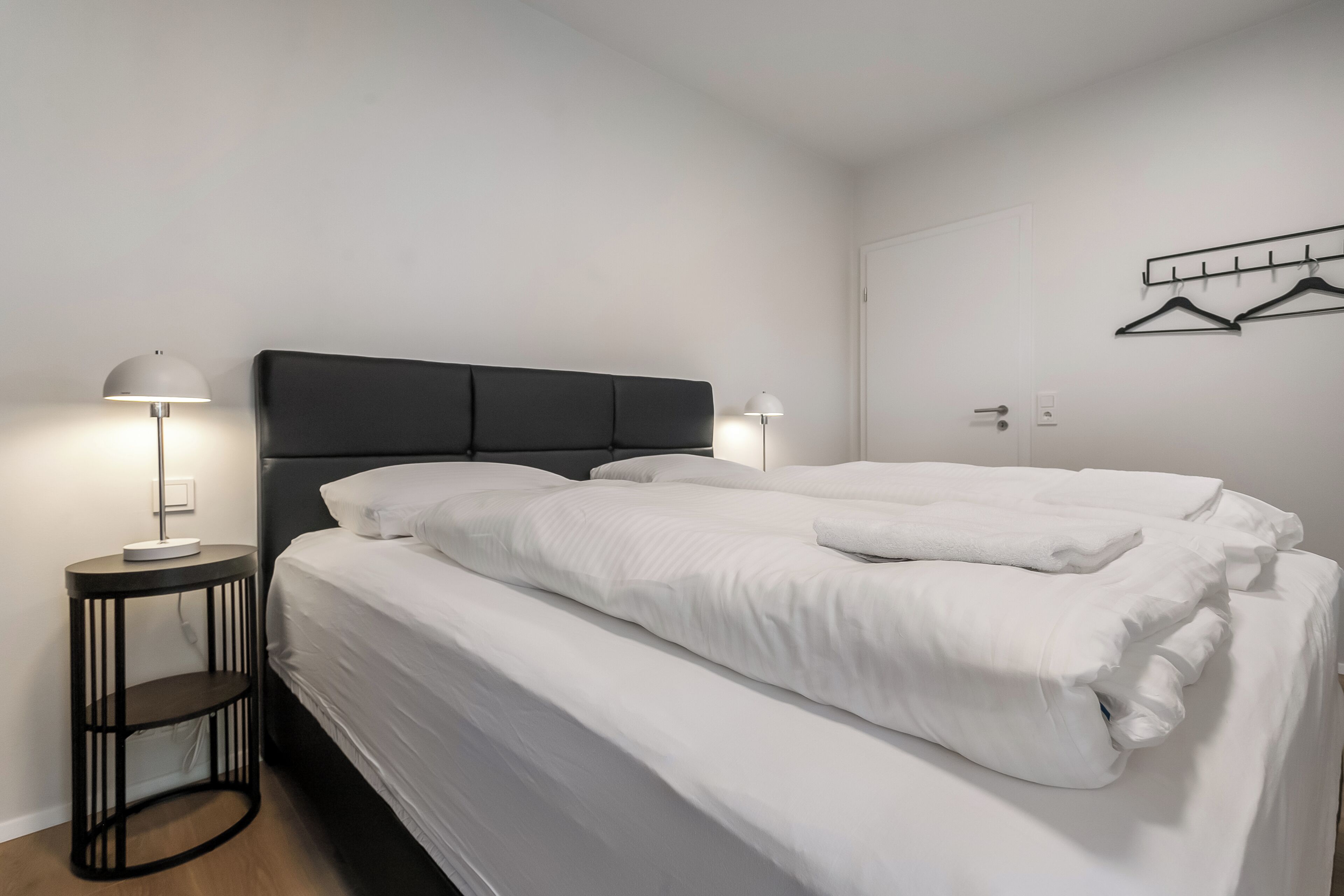 Et hotelværelse med en dobbeltseng, to sengeborde, to sengetåget lampe og et knagered med tøjhenger.