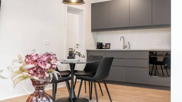 Una cocina moderna con armarios oscuros, un comedor con mesa y sillas negras, y un florero con flores.