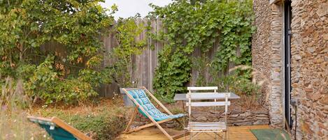 A wooden deck with two lounge chairs and a small table, surrounded by a stone wall and a wooden fence.