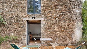 A rustic stone building with a wooden door, a small table, and two folding chairs outside. - "Chambre Terrasse" Guest Room with Shared Terrace, Garden, and Wi-Fi (La Possonnière)
