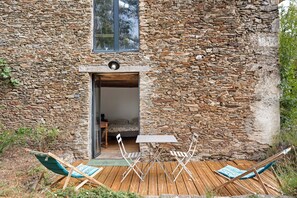 A rustic stone building with a wooden door, a small table, and two folding chairs outside.