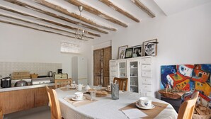 A dining area with a table set for two, a kitchen in the background, and a colorful painting on the wall.