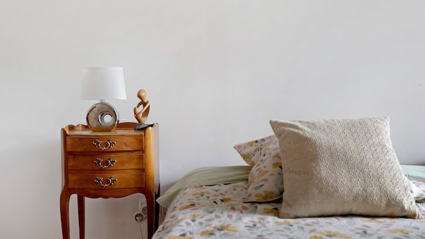 A bedroom with a wooden nightstand, a lamp, a decorative sculpture, and a floral-patterned bed with a pillow.