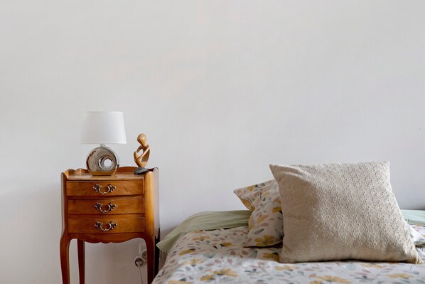A bedroom with a wooden nightstand, a lamp, a decorative sculpture, and a floral-patterned bed with a pillow.