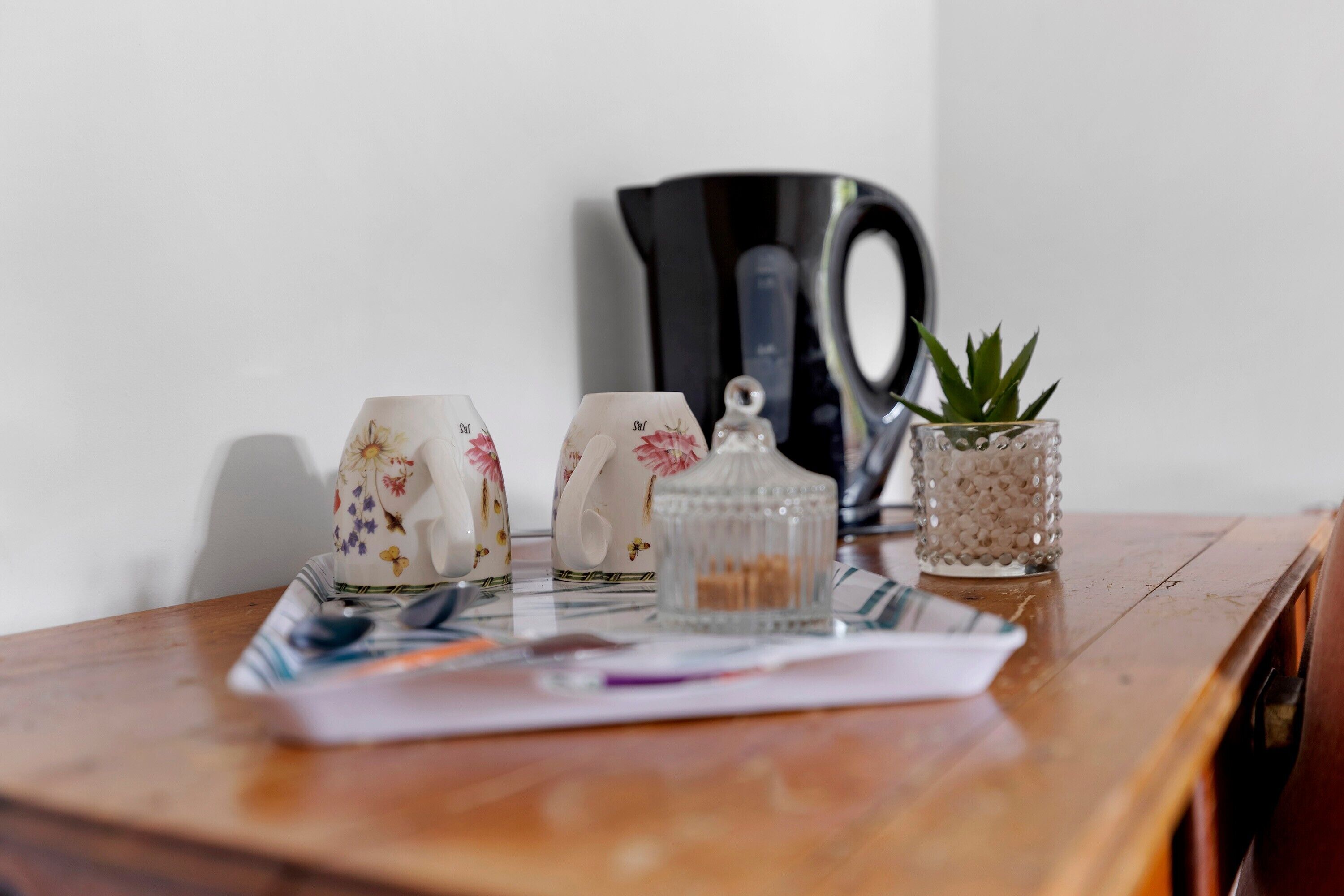 Una mesa de madera con una tetera, dos tazas, un frasco de vidrio y una pequeña planta en maceta.