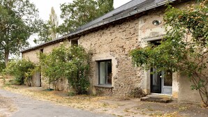 A rustic stone building with a sloped roof, a front door, and a window.