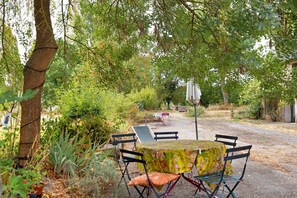 An outdoor seating area with a table and chairs, surrounded by greenery and trees.