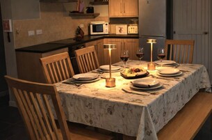 Mesa para cuatro personas dispuesta con mantel floreado, dos sillas y una lámpara encendida.