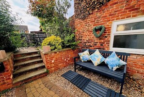 A brick wall with a heart-shaped wreath, a bench with cushions, and a small garden area with steps leading up to a window.