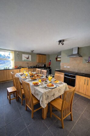 A dining area with a table set for breakfast, surrounded by wooden chairs, in a kitchen with wooden cabinets and a tiled floor. - The Old Shop at Savile House (Ollerton)