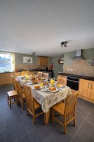 A dining area with a table set for breakfast, surrounded by wooden chairs, in a kitchen with wooden cabinets and a tiled floor.