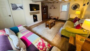 Una sala de estar acogedora con chimenea, vigas de madera, un sofá, un sillón verde y una estantería.