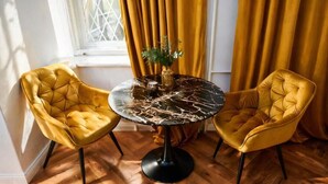 Una habitación con una mesa redonda, dos sillas amarillas, un florero con plantas verdes y cortinas amarillas.