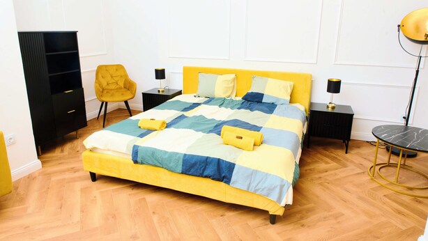 Una cama con colcha, dos mesitas de noche, una silla, un armario y una lámpara de pie.