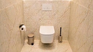 Un baño con inodoro, un bote de basura y un escobillón.