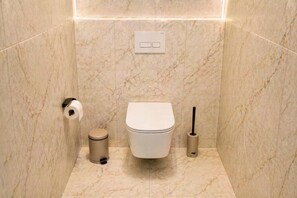 A bathroom with a toilet, a trash can, and a toilet brush. - Refined Central Sanctuary – Perfect Romantic Getaway by the River – 701 (Budapest)
