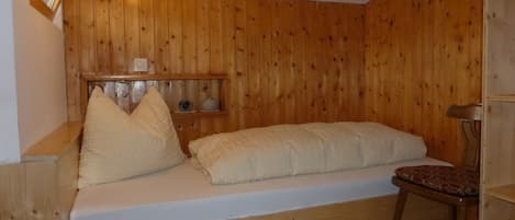A small, cozy room with a wooden bunk bed, a wooden shelf with decorative items, and a single chair.