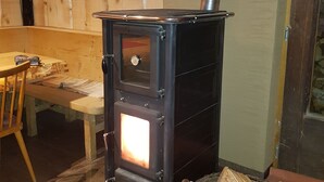 A wood-burning stove with a chimney, a wooden table, and a basket of firewood. - Schwendehof Vacation Home, Rental Unit 1 (Fontanella)
