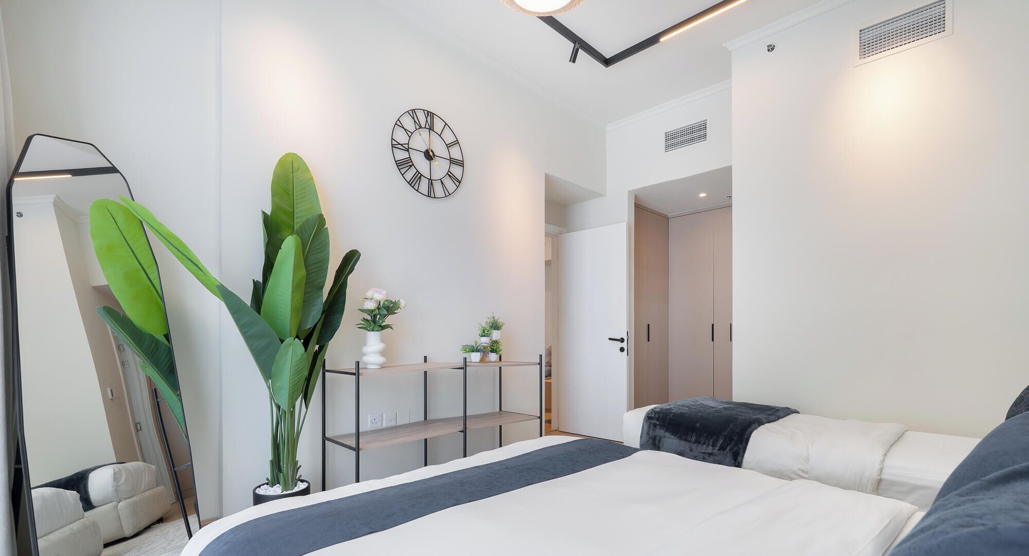 Un dormitorio moderno con cama, una planta grande, un reloj de pared y un armario.