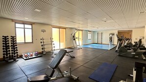 Een fitnessruimte met diverse trainingsapparaten, een blauw matgedeelte en een muur met de tekst 'NO PAIN NO GAIN'.