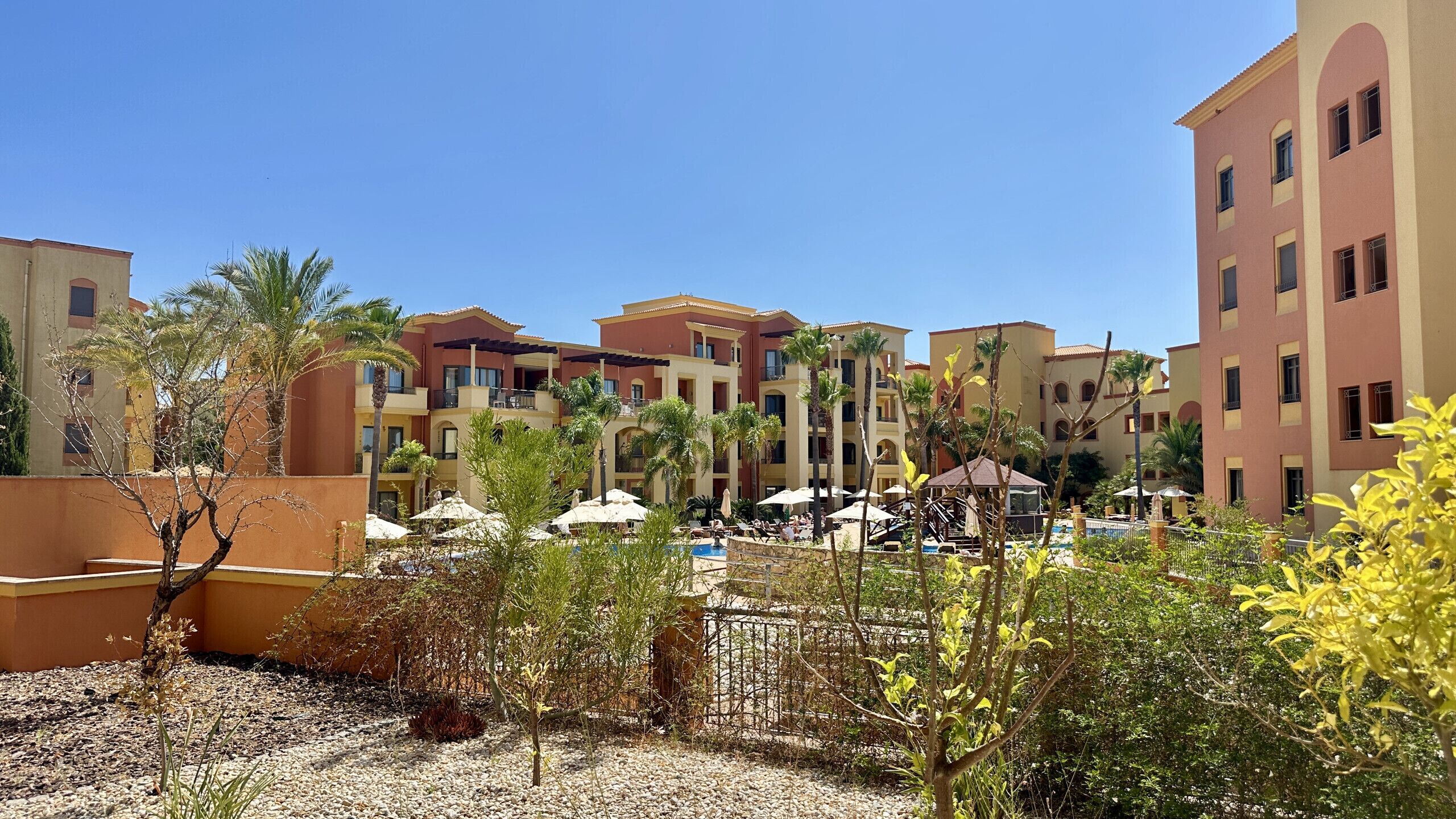 A resort with multiple-story buildings, outdoor seating areas, and a pool.