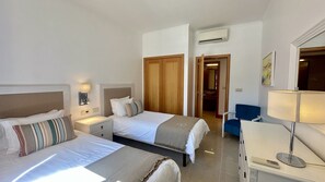 A hotel room with two beds, a desk, a chair, a bathroom with a mirror, and an air conditioning unit. - Vilamoura Residences | Swimming Pools | Gym | 6 People (Vilamoura)