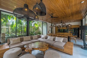 A modern interior with a sectional sofa, round coffee table, and hanging wicker pendant lights. - Villa Yuka (Ubud)