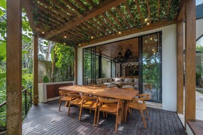 An outdoor dining area with a wooden table and chairs, a pergola with climbing plants, and a view of the surrounding greenery. - Villa Yuka (Ubud)