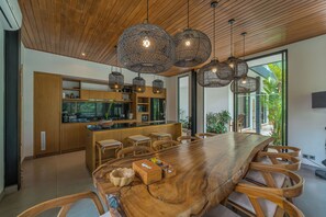 A modern kitchen with wooden cabinets, a large island, and hanging pendant lights. - Villa Yuka (Ubud)