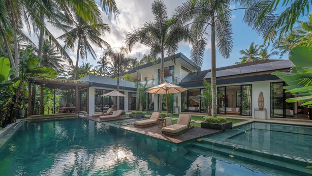 A modern pool area with lounge chairs and umbrellas, surrounded by lush tropical vegetation. - Villa Yuka (Ubud)