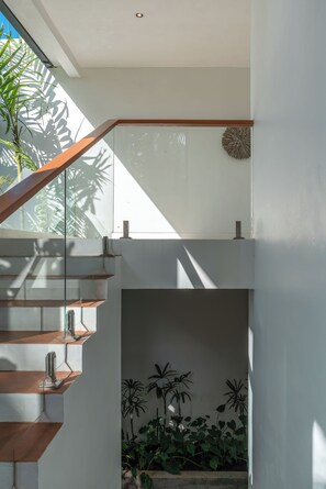 A modern staircase with glass railings and a wooden handrail, leading to an upper level. - Villa Yuka (Ubud)