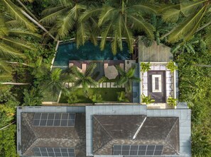 An aerial view of a modern resort with a swimming pool surrounded by lush greenery, including palm trees. - Villa Yuka (Ubud)