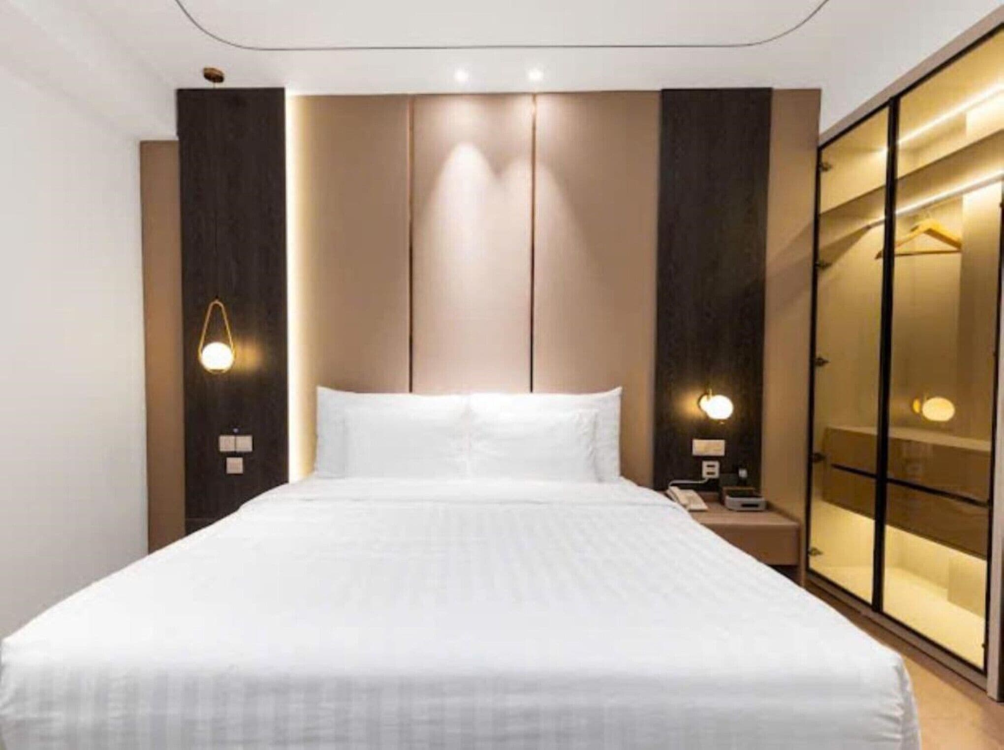 Una habitació d'hotel amb un llit gran, petjacs, una taula de nit i un armari amb mirall.