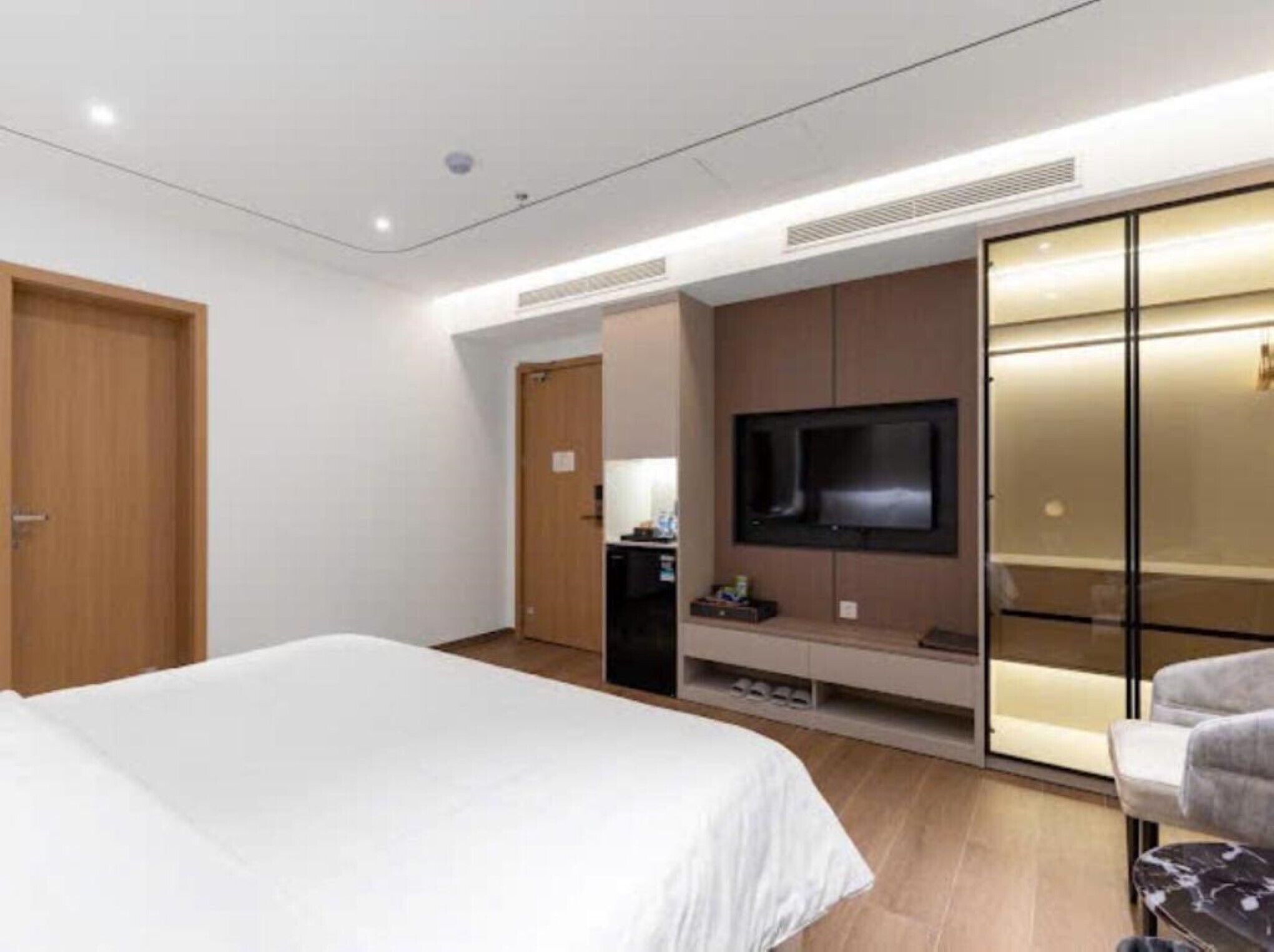 Una habitación de hotel moderna con una cama grande, un televisor montado en la pared y un armario con puertas correderas.