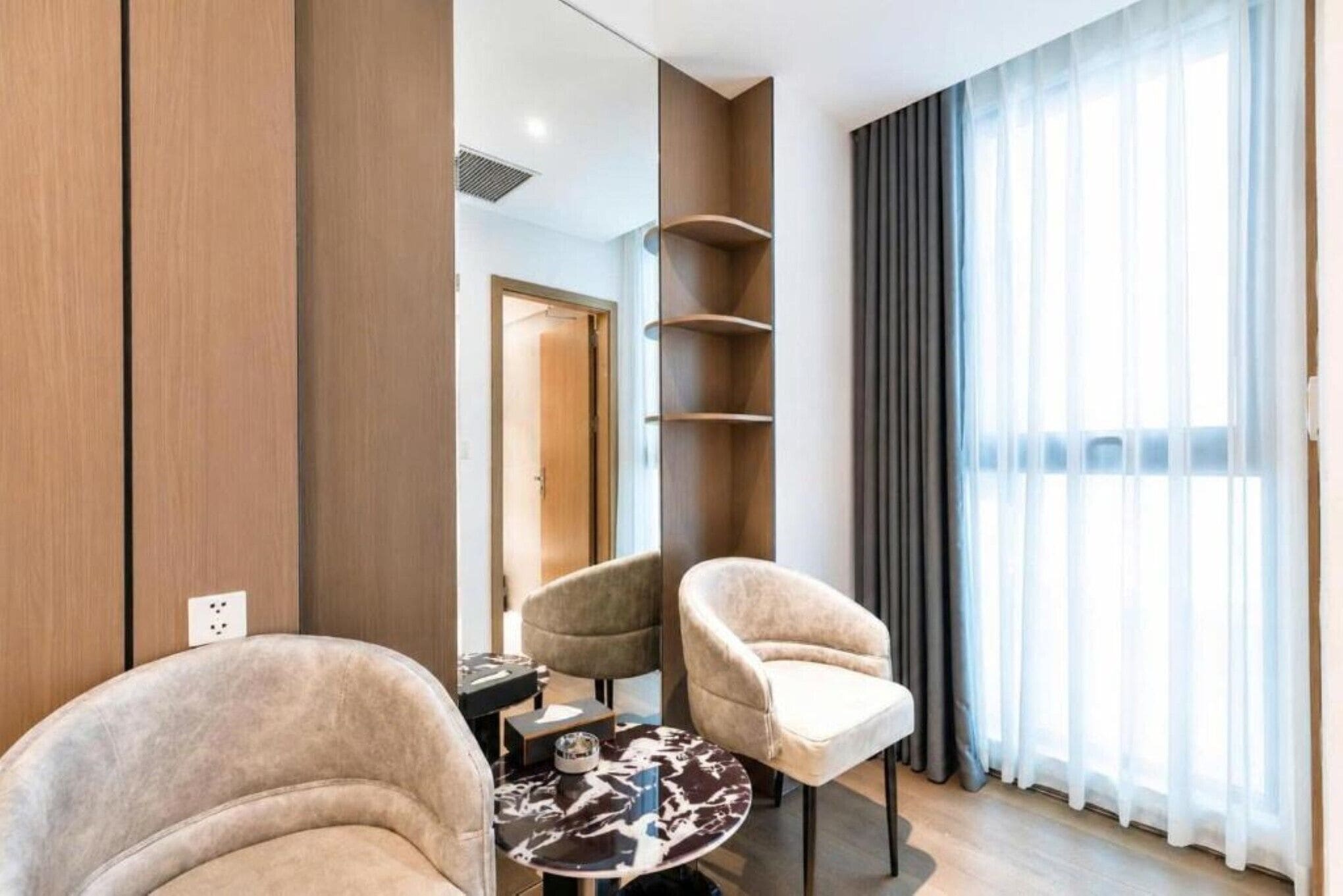 A modern hotel room with a sofa, armchairs, a coffee table, and a large window with curtains.