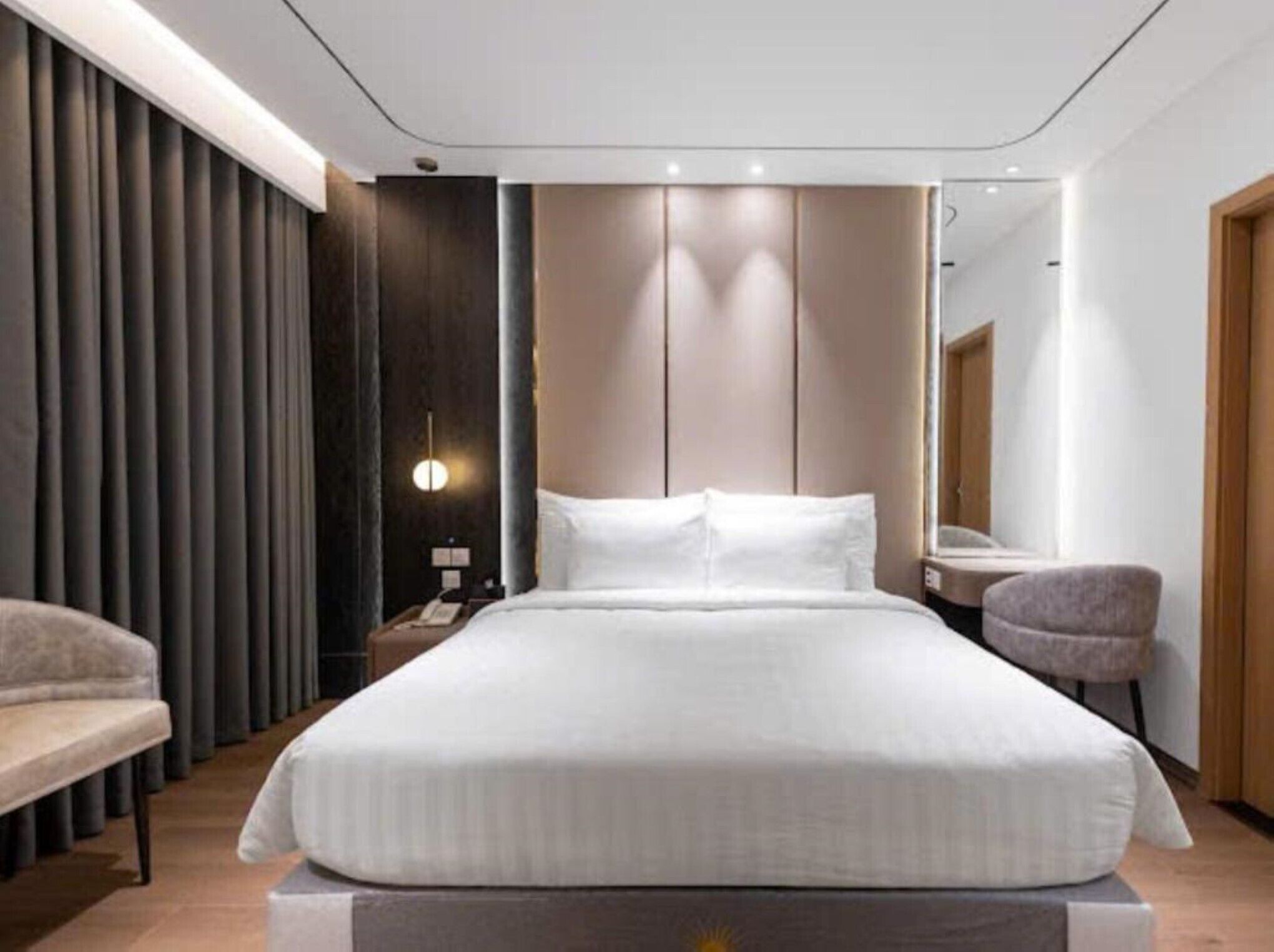 Una habitación de hotel moderna con una cama grande, mesitas de noche, una silla, un escritorio y un espejo.