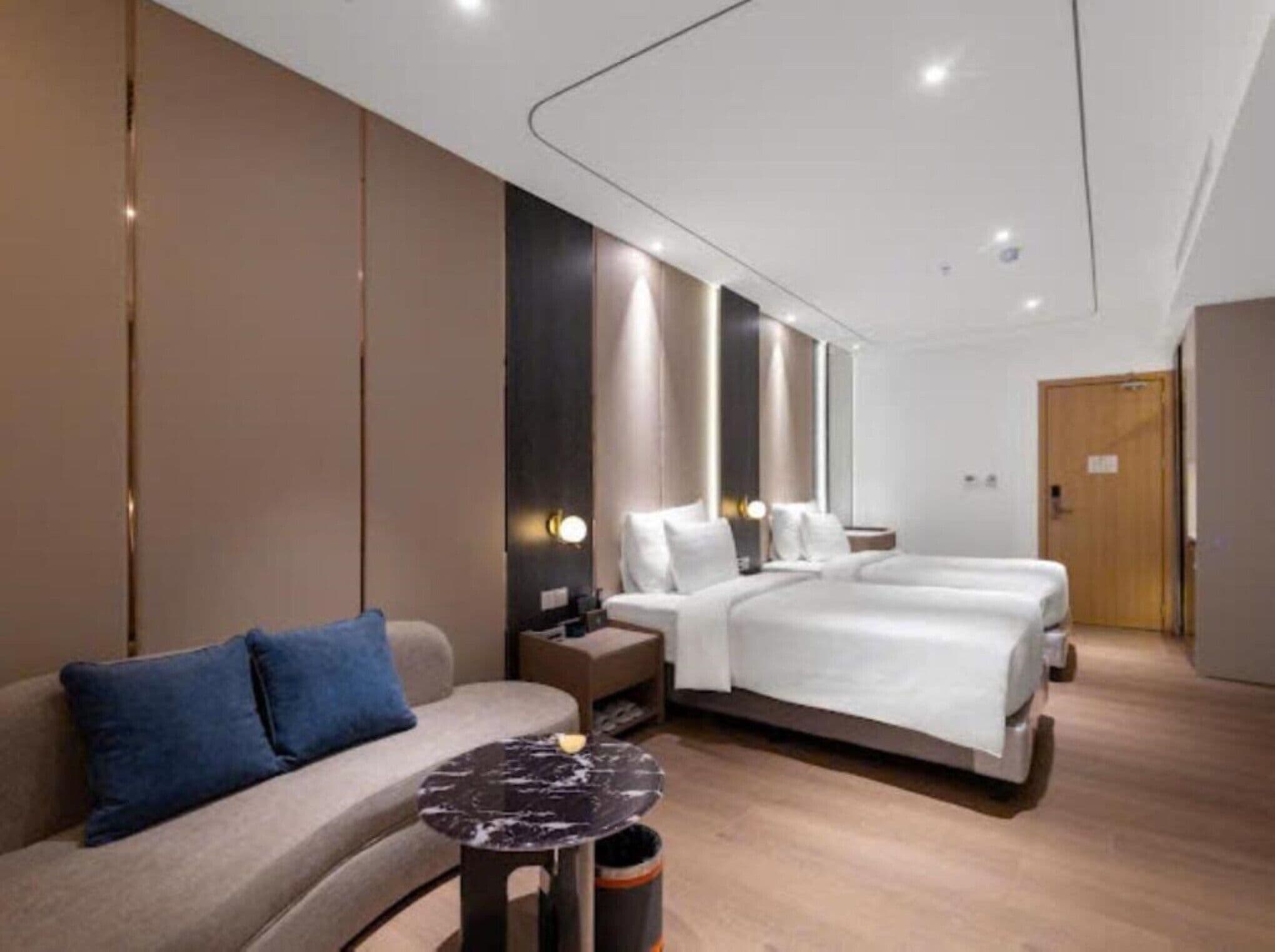 Ein modernes Hotelzimmer mit einer Sitzecke, einem kleinen runden Tisch, einem Bett mit weißer Bettwäsche und einem Nachttisch.