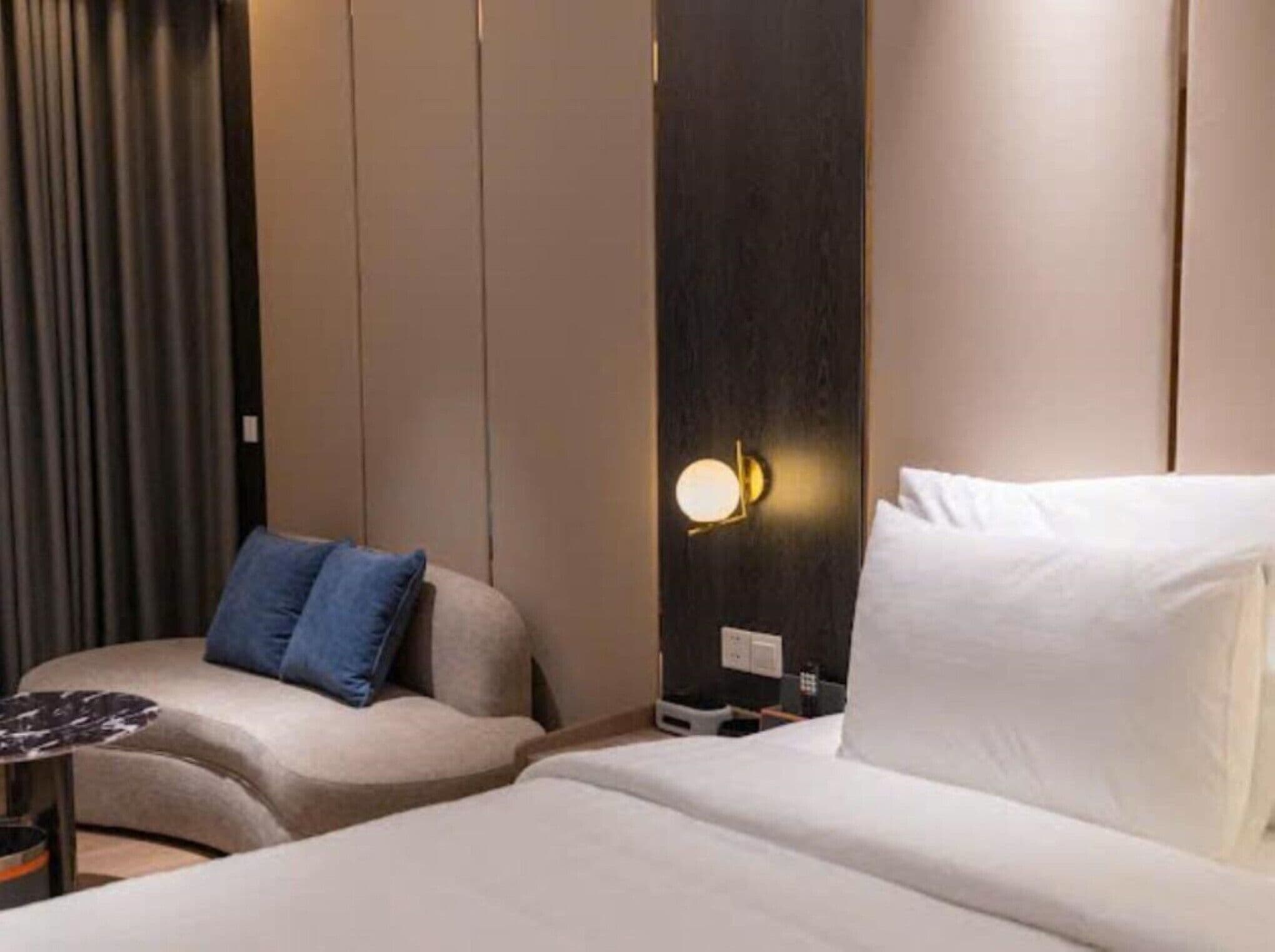 A hotel room with a bed, a sofa, and a nightstand with a lamp.