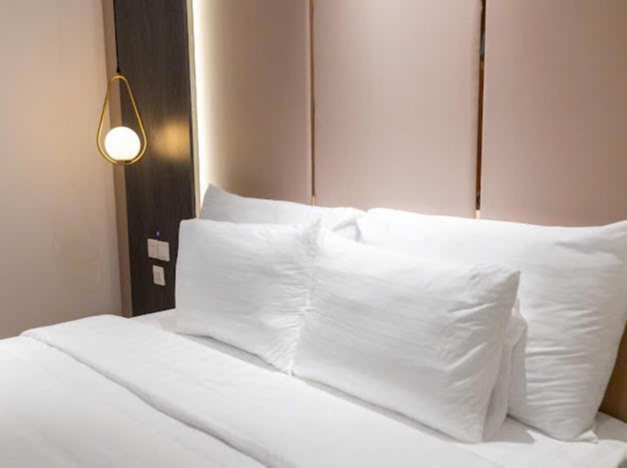 Una habitación de hotel con una cama bien hecha, una lámpara fijada a la pared y un cabecero de madera oscura.