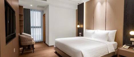 Habitación de hotel moderna con una cama grande, una mesita de noche con lámpara, una silla y un televisor montado en la pared.
