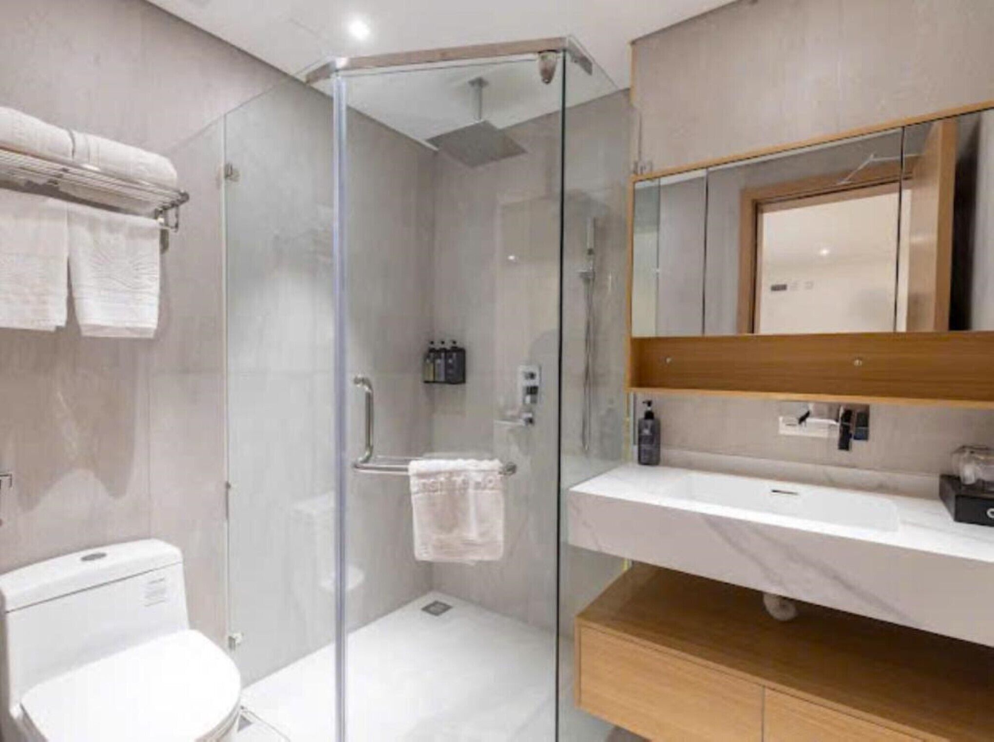 A modern bathroom with a glass shower enclosure, a white toilet, a sink with a mirror above it, and a towel rack with towels.