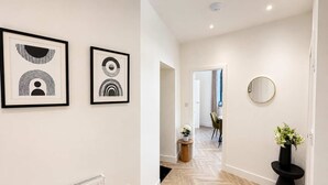 Un couloir avec un radiateur, des œuvres d’art encadrées, un miroir rond et une plante en pot.