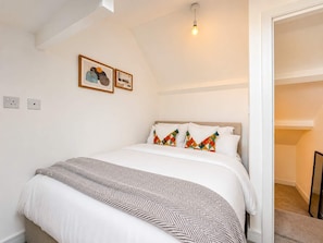 Un dormitorio con cama, cabecera, luz empotrada en la pared y puerta que da a otra habitación.