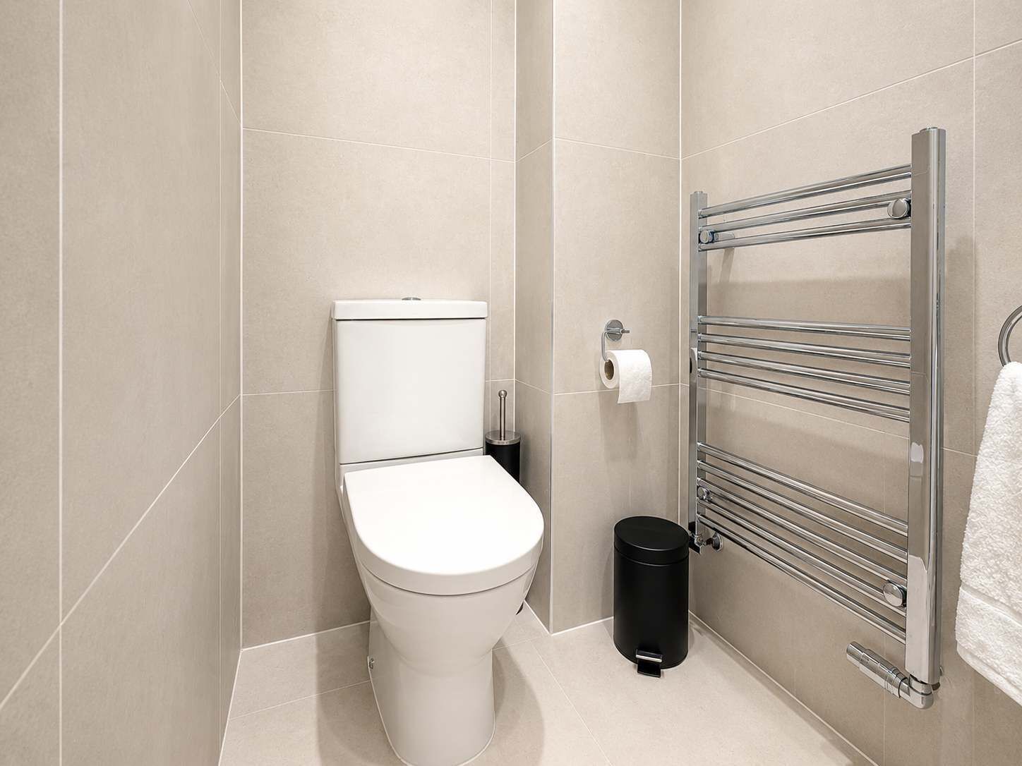 Et moderne badeværelse med toilet, skraldespand og håndklædestang.