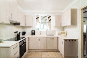A modern kitchen with light wood cabinets, a black stove, and a window above the sink. - Spacious Family Retreat with Two Houses & Private Pool (Javea)
