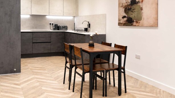 A modern kitchen with a dining area, featuring a herringbone floor pattern, a wooden dining table, and a single flower vase. - Modern 1BR - Sleeps 4 - Free Parking - Manchester (Manchester)