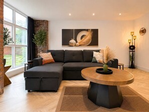 A modern living room with a sectional sofa, a round wooden coffee table, and a large window with curtains. - Modern 1BR - Sleeps 4 - Free Parking - Manchester (Manchester)
