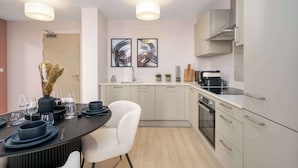 A modern kitchen with a dining area, featuring a stove, oven, and two framed abstract paintings. - Luxury VIEWS!  10th  Floor  2 Bed Apartment (Manchester)