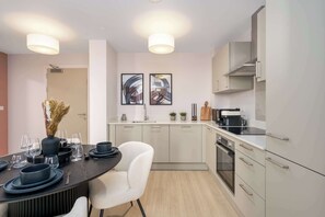 A modern kitchen with a dining area, featuring a stove, oven, and two framed abstract paintings. - Luxury VIEWS!  10th  Floor  2 Bed Apartment (Manchester)