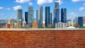 A city skyline with modern high-rise buildings, a brick wall in the foreground, and a clear blue sky. - Luxury VIEWS!  10th  Floor  2 Bed Apartment (Manchester)